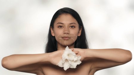 Photo for Beauty and skincare treatment creative concept. Closeup studio shot of attractive young model. Beautiful asian girl with long hair holding white flowers and smiling at the camera. - Royalty Free Image