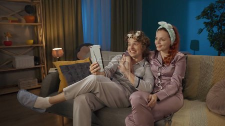 Photo for Beauty and healthy relationships advertisement concept. Portrait of young couple. Closeup of man and woman in pajamas sitting on the sofa in hairbands, talkin by video call on tablet. - Royalty Free Image