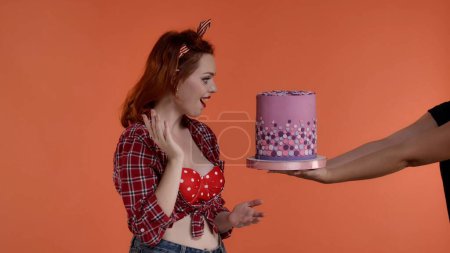 Photo for The shot features a young red-haired woman with brightly colored makeup against a red background. She looks at the gift box someone is handing her. Demonstrates joy, surprise, delight. Medium shot - Royalty Free Image