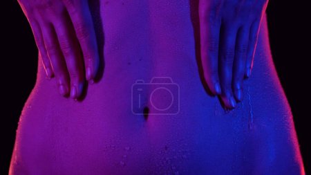 Photo for Skin texture and bodycare concept. Portrait of attractive young female model. Closeup shot of beautiful caucasian woman body part in neon light, touching belly area skin in waterdrops after bathing. - Royalty Free Image