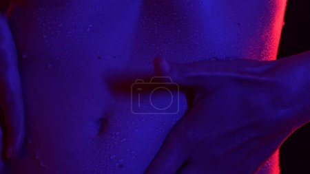 Photo for Skin texture and bodycare healthcare concept. Portrait of attractive young female model. Closeup beautiful caucasian woman body part in neon light, holding hand on tummy area, water drops after bath. - Royalty Free Image