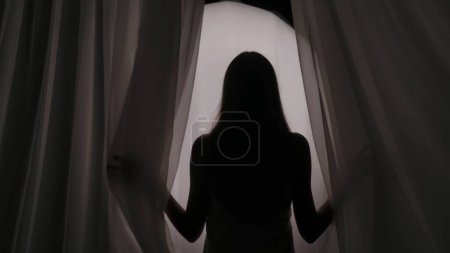 Photo for Medium shot of a young womans silhouette wrapped in a towel coming from behind the curtain, on a semi-transparent glowing background in a muffled light. Product advertisement, self-care routine. - Royalty Free Image