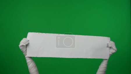 Foto de Detalle pantalla verde aislada croma clave foto captura momias manos sosteniendo un pedazo de papel vacío y en blanco. Halloween, maqueta y bandera para su promoción, publicidad. - Imagen libre de derechos