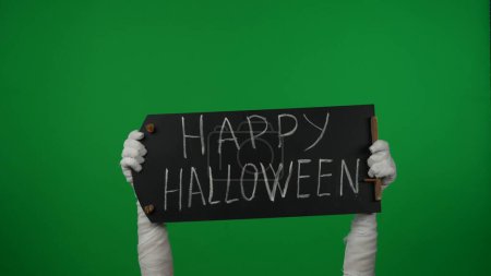Foto de Detalle pantalla verde aislada croma clave foto captura momias manos sosteniendo una pizarra negra con feliz halloween escrito en ella. Prepárate para tu clip de promoción o anuncio. - Imagen libre de derechos