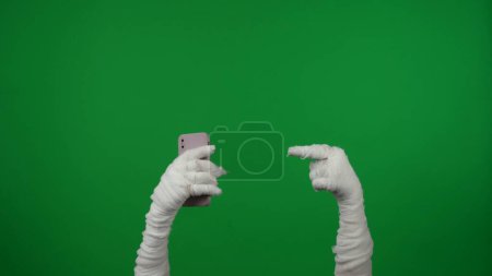Foto de Detalle pantalla verde aislada croma clave foto captura momias mano sosteniendo un teléfono inteligente y apuntando a ella para alentar a unirse o comprar. Prepárate, espacio de trabajo para tu clip de promoción o anuncio - Imagen libre de derechos