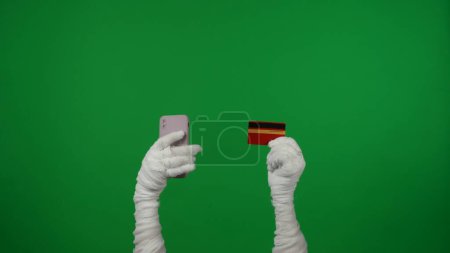 Foto de Pantalla verde croma clave foto captura momias manos sosteniendo un teléfono inteligente y una tarjeta de crédito en sus manos, animando a comprar, comprar un producto. Prepárate para tu clip de promoción o anuncio. - Imagen libre de derechos