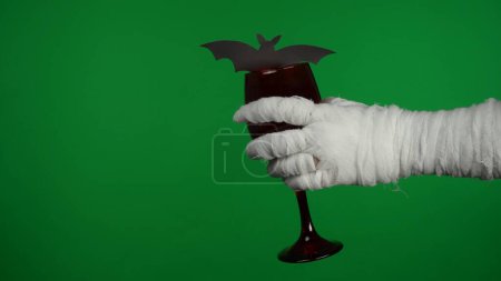 Photo for Detail green screen isolated chroma key photo capturing mummys hand holding a glass with beverage. The glass is decorated with a bat. Mock up, workspace for your promotion clip or advertisement. - Royalty Free Image