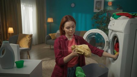Photo for Medium-full shot. Redhead woman unloading washed laundry from the washing machine, checking the clothes for any stains left. Household appliances, chores, promotion and advertisement. - Royalty Free Image