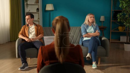 Photo for Married couple sitting on different sides of the couch in front of the female therapist. A man and a woman in a quarrel avoid eye contact. Crisis in relationships - Royalty Free Image