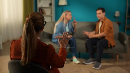 Photo for Back view of a female therapist, against a blurred background of a couple arguing. The therapist is trying to calm a man and woman blaming each other for problems. A married couple sitting on a couch - Royalty Free Image