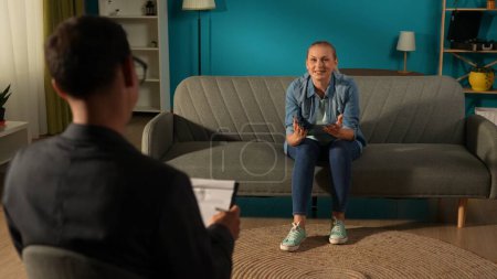 Photo for Cheerful, happy woman sitting on couch in front of male psychotherapist. The woman is overwhelmed with positive emotions and gratitude to the specialist for help. Psychotherapy was successful - Royalty Free Image