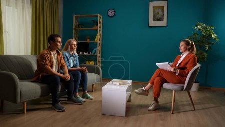 Photo for A psychotherapist helps a couple improve their relationship. A man and a woman sitting on a couch in front of a therapist with a clipboard. Side view. Crisis of relationships in family life - Royalty Free Image