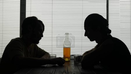 Foto de Las imágenes muestran a dos jóvenes sentados en una mesa en un café. Hay una botella de alcohol al lado de ellos, están hablando de algo y van a beber. Demuestra adicción al alcohol. - Imagen libre de derechos