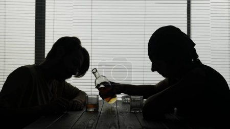 Photo for The shot shows two young guys sitting in an establishment, a cafe. One is pouring alcohol in a glass. They demonstrate socializing, intoxication. Alcohol addiction, interlocutor. Medium video. - Royalty Free Image