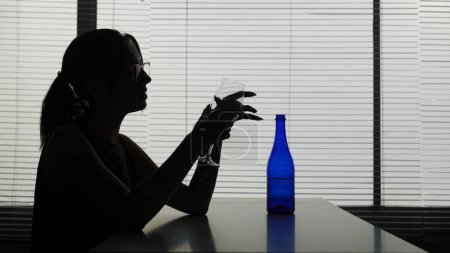 Photo for A young woman with glasses is sitting at a table in a cafe thinking about something, a bottle is next to her. She holds a glass with alcohol in her hands and looks at it. Demonstrates alcoholism. - Royalty Free Image