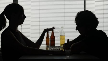 Photo for A man and woman are at a table in surroundings bottles. On a table wineglasses cost with an alcohol. Demonstrate a quarrel he drinks an alcohol. A woman lights a cigarette and says on with him. - Royalty Free Image
