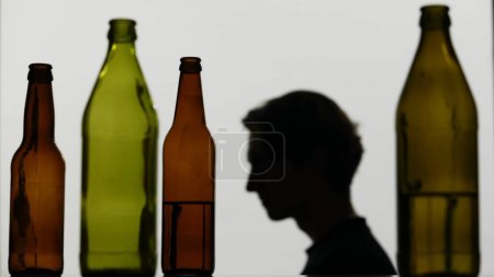 Photo for A close-up of multicolored empty bottles on a white background. In the background is a silhouette of a man. He sits sideways to the camera and looks somewhere. Medium shot. - Royalty Free Image