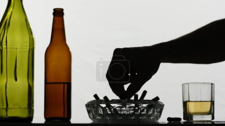Photo for In the close-up shot, the camera moves showing empty, dissipated, glass bottles with alcohol, ash with cigarettes and a glass filled with alcohol. Shows bad habits, addiction. Medium shot. - Royalty Free Image