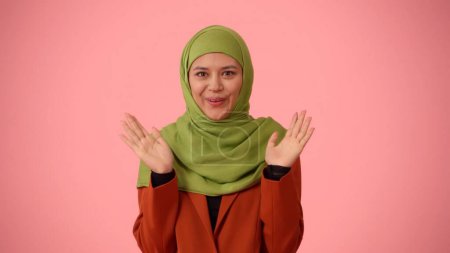 Foto de Foto aislada de tamaño mediano que captura a una atractiva joven con un hiyab, velo. Ella está expresando asombro y emoción, levantando las manos. Lugar para su anuncio, cultural, diversidad. - Imagen libre de derechos