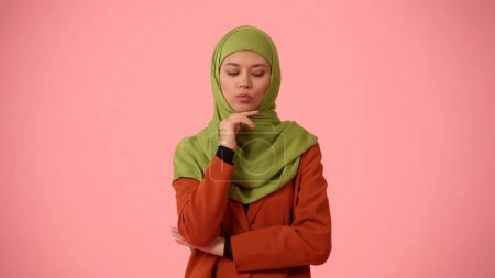 Photo for Medium-sized isolated photo capturing an attractive young woman wearing a hijab, veil. She raised her hand to her chin as if she is thinking of a plan. Place for your advertisement, cultural - Royalty Free Image