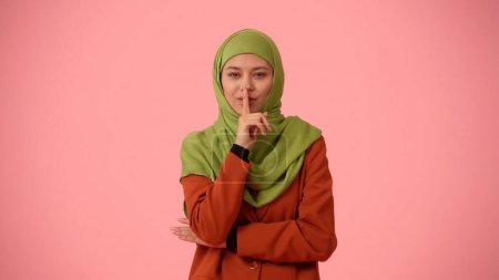 Téléchargez les photos : Photo isolée de taille moyenne capturant une jolie jeune femme portant un hijab, voile. Elle a l'air sournoise, sournoise, couvrant sa bouche, racontant un secret. Place pour votre publicité, culturel, diversité. - en image libre de droit