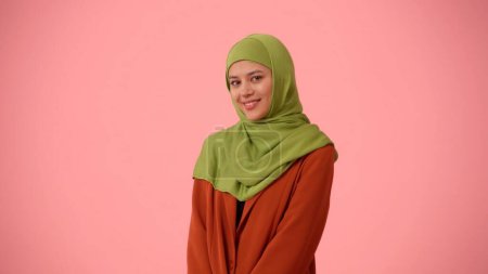 Foto de Foto aislada de tamaño mediano que captura a una atractiva joven con un hiyab, velo. Se apoya la cabeza en el hombro, actuando lindo y tímido. Lugar para su anuncio, cultural, diversidad. - Imagen libre de derechos