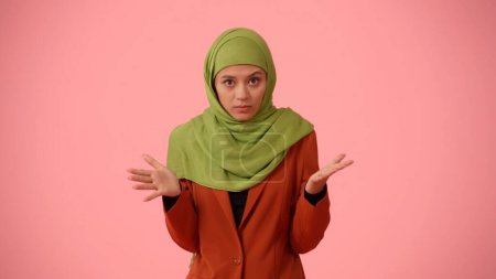 Foto de Foto aislada de tamaño mediano que captura a una atractiva joven con un hiyab, velo. Ella está estremeciendo sus manos, mirando a la cámara con ira. Lugar para su anuncio, cultural, diversidad. - Imagen libre de derechos