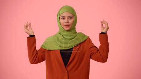 Foto de Foto aislada de tamaño mediano que captura a una atractiva joven con un hiyab, velo. Ella mira a la cámara, sosteniendo sus manos en gestos de mudra. Lugar para su anuncio, cultural, diversidad. - Imagen libre de derechos