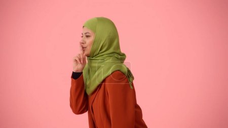 Téléchargez les photos : Photo isolée de profil latéral moyen capturant une jolie jeune femme portant un hijab, voile. Elle se tait sournoisement comme si elle gardait un secret. Place pour votre publicité, culturel, diversité. - en image libre de droit