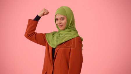 Photo for Medium-sized isolated photo capturing an attractive young woman wearing a hijab, veil. She is showing her muscles, expressing confidence. Place for your advertisement, cultural diversity, woman power. - Royalty Free Image