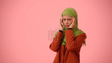 Téléchargez les photos : Photo isolée de taille moyenne capturant une jolie jeune femme portant un hijab. Elle masse les tempes de sa tête comme si elle avait mal à la tête. Publicité pharmaceutique, culturelle, diversité. - en image libre de droit