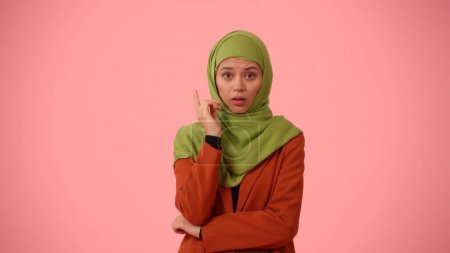 Foto de Foto aislada de tamaño mediano que captura a una atractiva joven con un hiyab, velo. Levantó el dedo en el aire como si se le ocurriera una idea. Lugar para su anuncio, diversidad cultural - Imagen libre de derechos