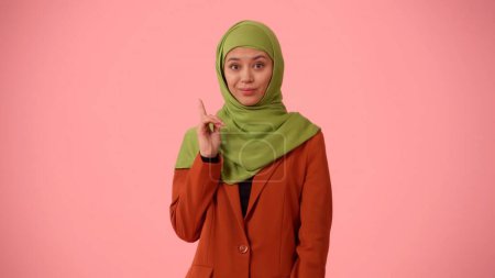 Téléchargez les photos : Photo isolée de taille moyenne capturant une jolie jeune femme portant un hijab, voile. Elle leva le doigt en l'air comme si elle avait eu une idée. Place pour votre publicité, diversité culturelle - en image libre de droit