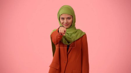 Photo for Medium-sized isolated photo capturing an attractive young woman wearing a hijab, veil. She is poiting at the camera, calling you to join up. Place for your advertisement, mock up, promotional. - Royalty Free Image
