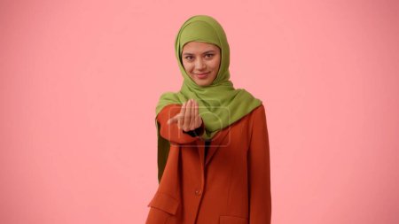 Photo for Medium-sized isolated photo capturing an attractive young woman wearing a hijab, veil. She is calling you with her hand encouraging you to join. Place for your advertisement, mock up, promotional. - Royalty Free Image