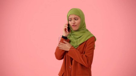 Téléchargez les photos : Photo isolée de taille moyenne capturant une jolie jeune femme portant un hijab, voile. Elle parle au téléphone, discute avec quelqu'un. Place pour votre publicité, culturel, diversité. - en image libre de droit