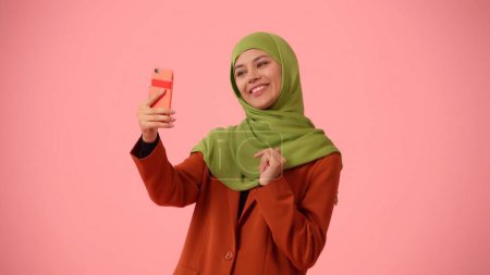 Téléchargez les photos : Photo isolée de taille moyenne capturant une jolie jeune femme portant un hijab, voile. Elle enregistre elle-même, a un vidéocall et parle activement. Lieu de publicité, de culture, de diversité. - en image libre de droit