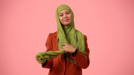 Foto de Foto aislada de tamaño mediano que captura a una joven atractiva que está usando o quitándose un hijab, velo con una sonrisa en la cara. Lugar para su anuncio, diversidad cultural, libertad de elección - Imagen libre de derechos