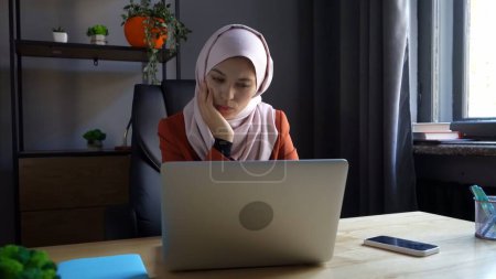 Foto de Foto de tamaño mediano que captura a una atractiva joven con un hiyab, velo. Ella está trabajando o estudiando en su portátil, pensando en algo. Diversidad cultural, empleo y educación, publicidad. - Imagen libre de derechos