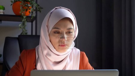 Téléchargez les photos : Photo rapprochée capturant une jolie jeune femme portant un hijab, voile. Elle travaille ou étudie sur son ordinateur portable, pensant à quelque chose. Diversité culturelle, emploi et éducation, publicité. - en image libre de droit