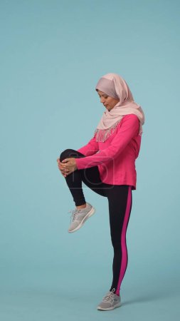 Photo for Full-sized isolated photo capturing an attractive young woman wearing a sportswear and a hijab, sheila. She is exercising, stretching, warming up. Place for your advertisement, promotional, sport. - Royalty Free Image