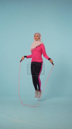 Foto de Foto aislada de tamaño completo que captura a una atractiva joven con ropa deportiva y un hiyab, Sheila. Ella está usando una cuerda de salto, saltando. Lugar para la publicidad, promocional, perder peso. - Imagen libre de derechos