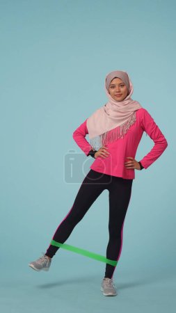 Photo for Full-sized isolated photo capturing an attractive young woman wearing a sportswear and a hijab, sheila. She is exercising with a rubber band. Place for your advertisement, mock up, promotional, sport. - Royalty Free Image