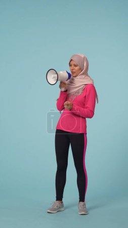 Photo for Full-sized isolated half turn photo capturing an attractive young woman wearing a sportswear and a hijab, sheila. She is actively speaking in a rupor. Place for your advertisement, promotional, sport. - Royalty Free Image