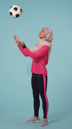 Photo for Full-sized isolated photo capturing an attractive young woman wearing a sportswear and a hijab, sheila. She is tossing, throwing the ball up. Place for your advertisement, mock up, promotional, sport. - Royalty Free Image