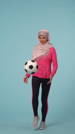 Foto de Foto aislada de tamaño completo que captura a una atractiva joven con ropa deportiva y un hiyab, Sheila. Está pateando la pelota. Lugar para tu anuncio, maqueta, promoción, deporte. - Imagen libre de derechos