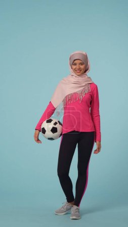 Foto de Foto aislada de tamaño completo que captura a una atractiva joven con ropa deportiva y un hiyab, Sheila. Ella sostiene una pelota de fútbol. Lugar para tu anuncio, maqueta, promoción, deporte. - Imagen libre de derechos