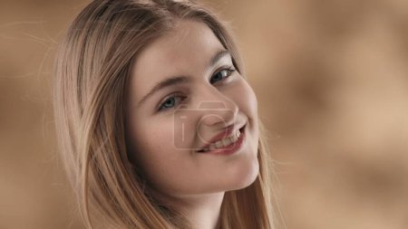 Photo for A close-up of a young blonde-haired woman against a stained background. With her head slightly turned and tilted, she looks at the camera and smiles. The wind is blowing on her, developing her hair. - Royalty Free Image