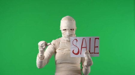Photo for Green screen isolated chroma key photo capturing a creepy mummy pointing at the piece of paper with a word sale written on it in capitals. Mock up for your promotion clip or product advertisement. - Royalty Free Image