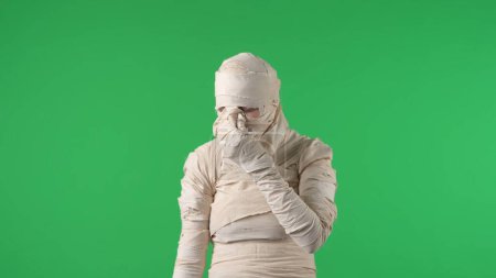 Photo for Green screen isolated chroma key photo capturing a mummy holding its nose, squinting and turning away as if its stinky. Halloween mock up, workspace for your promotion or advertisement. - Royalty Free Image